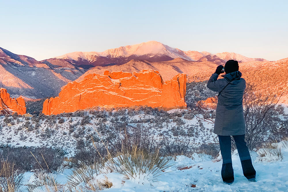 A woman on a hike taking a picture of the snowy Rocky mountains